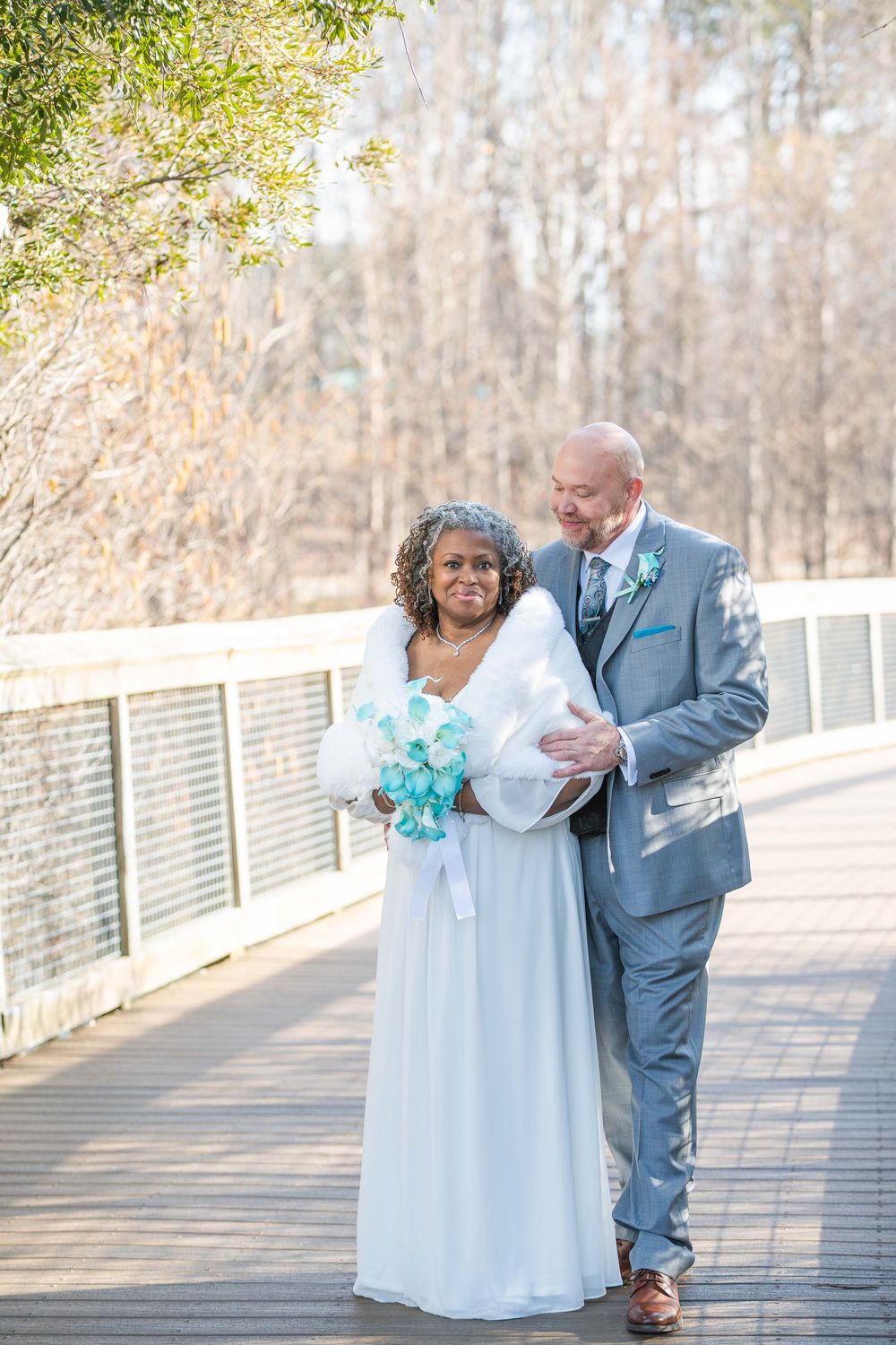 A happy couple in wedding attire share a tender moment on a wooden bridge surrounded by trees on their special day. Rhodes Jordan's Park.