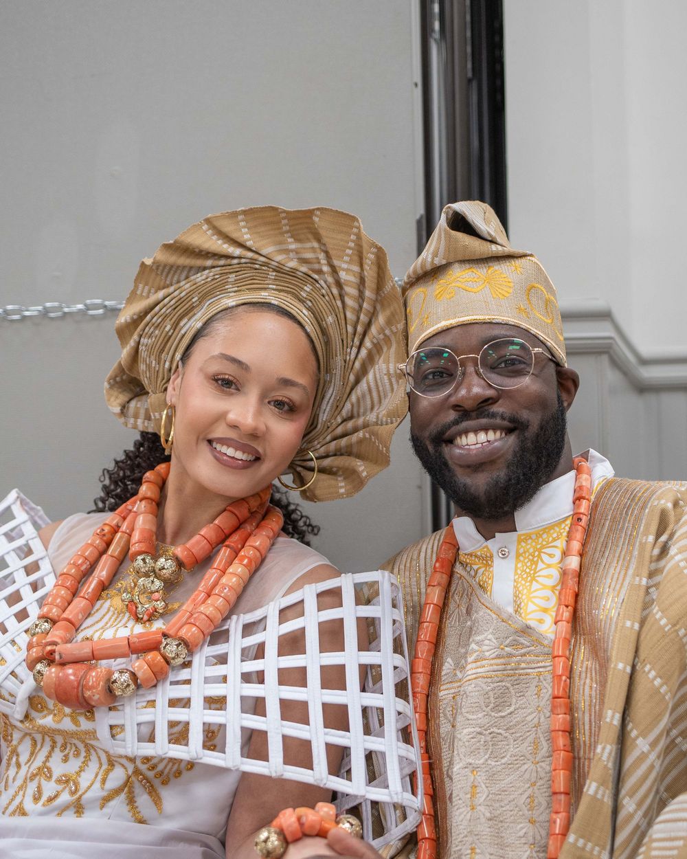 A couple in traditional African wedding attire with orange beaded necklaces pose together in a series of celebratory photos.