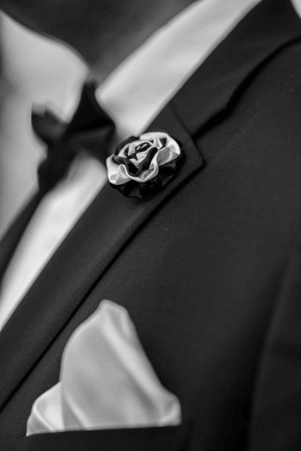 Close-up of black and white boutonniere flower pin on formal suit jacket.