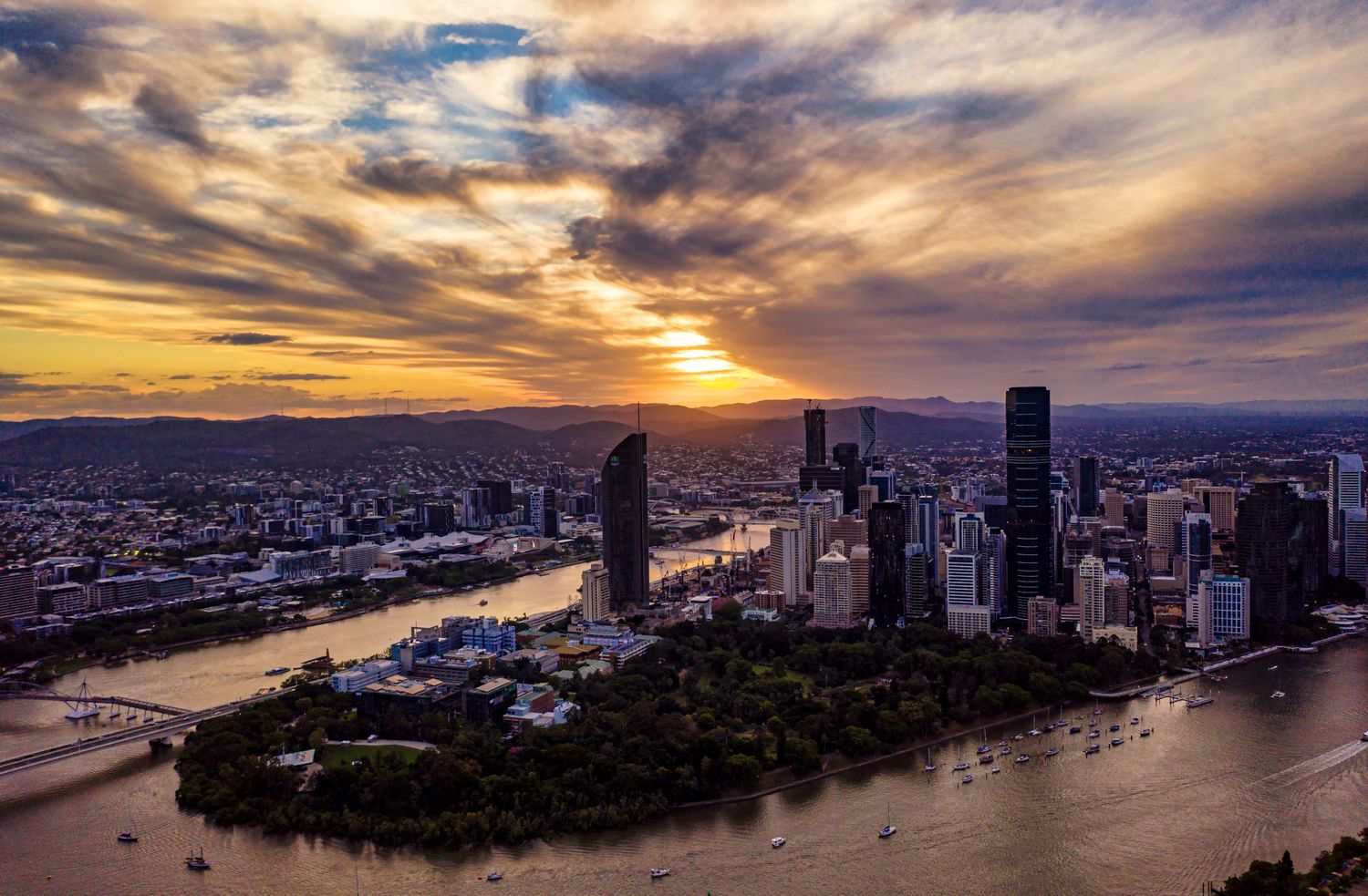 Stunning sunset over Brisbane city skyline with river winding around peninsula and skyscrapers.
