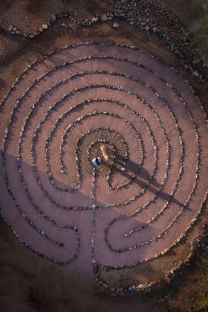 Time-lapse sequence showing the creation of a spiral stone labyrinth pattern on brown earth.