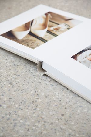White photo album open to page showing elegant bridal shoes and wedding details on textured concrete surface.