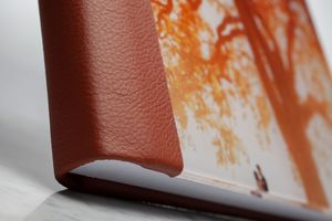 Closeup detail of brown leather book cover corner against blurred orange and white background.