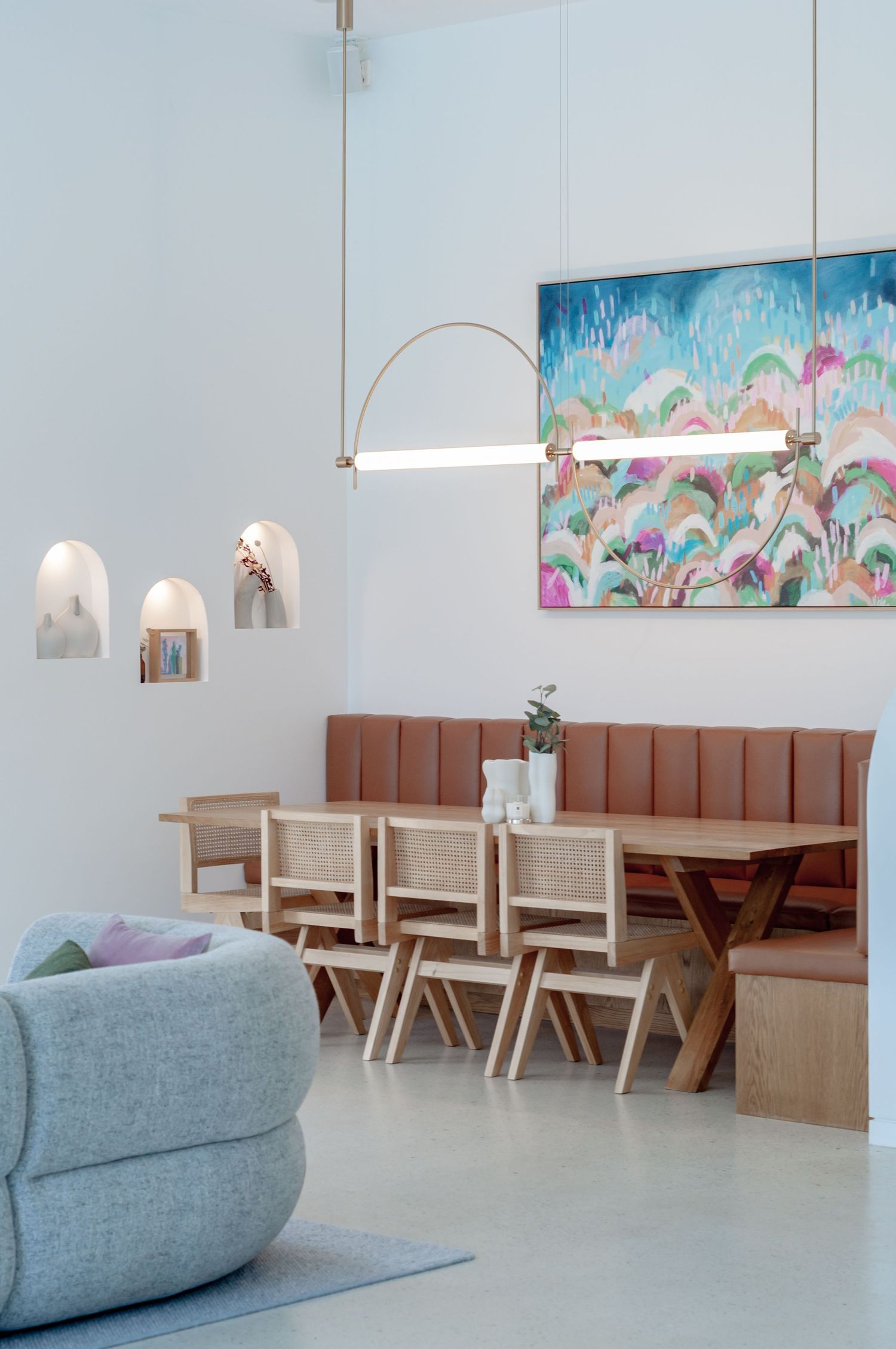 Modern restaurant interior with colorful wall art, leather banquette seating, and hanging pendant lights.