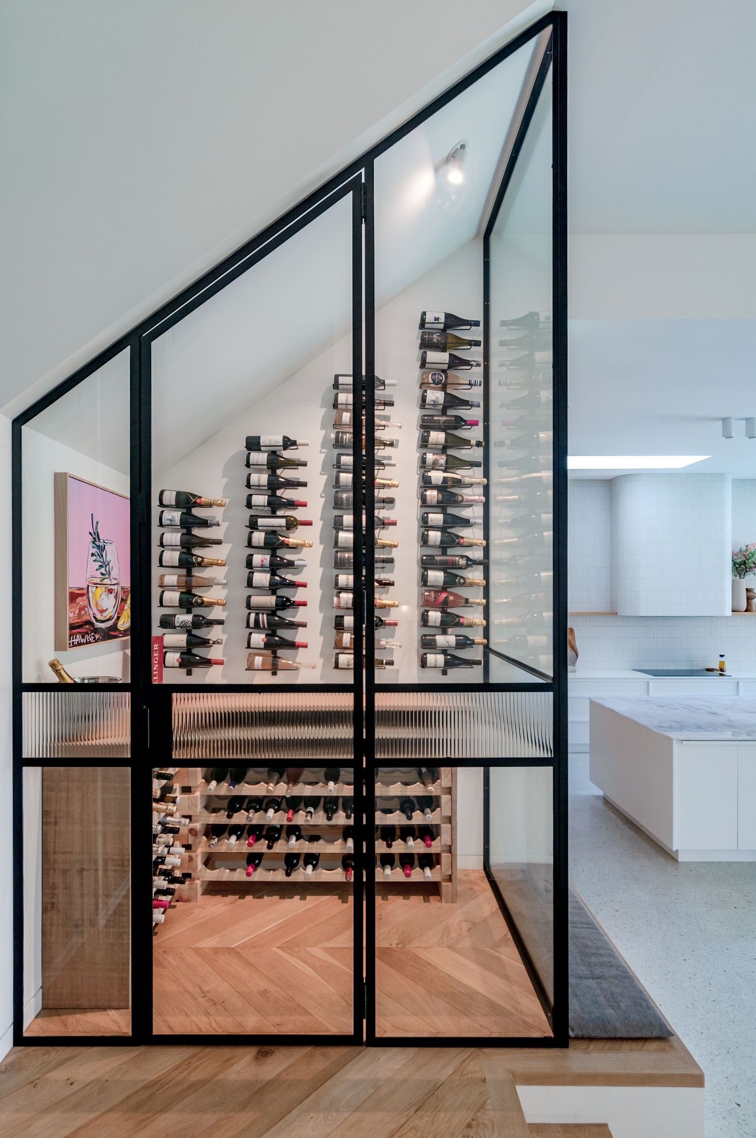 Modern wine cellar with black-framed glass walls features a chevron wood floor and wall-mounted wine bottle storage display.