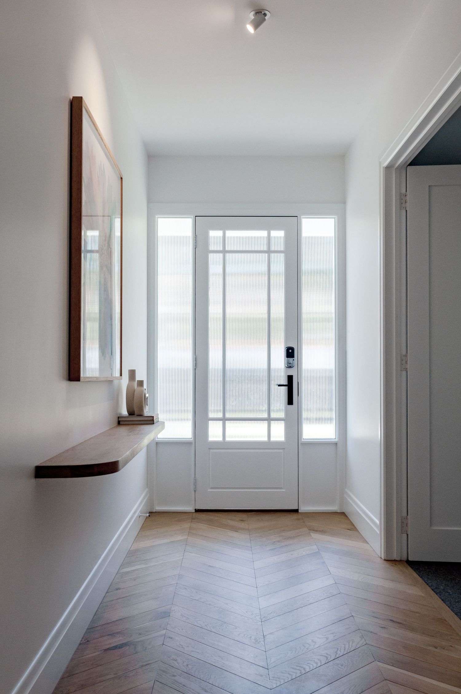 Bright white entryway with herringbone wood flooring and glass-paneled front door featuring minimalist decor.