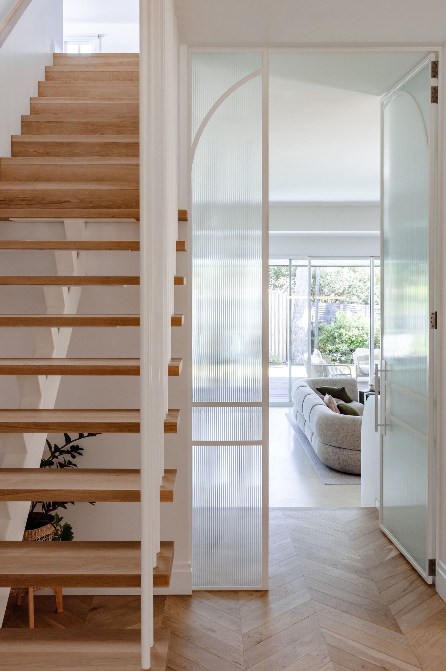 Modern floating wooden staircase with white walls and frosted glass partitions leading to a bright living space.