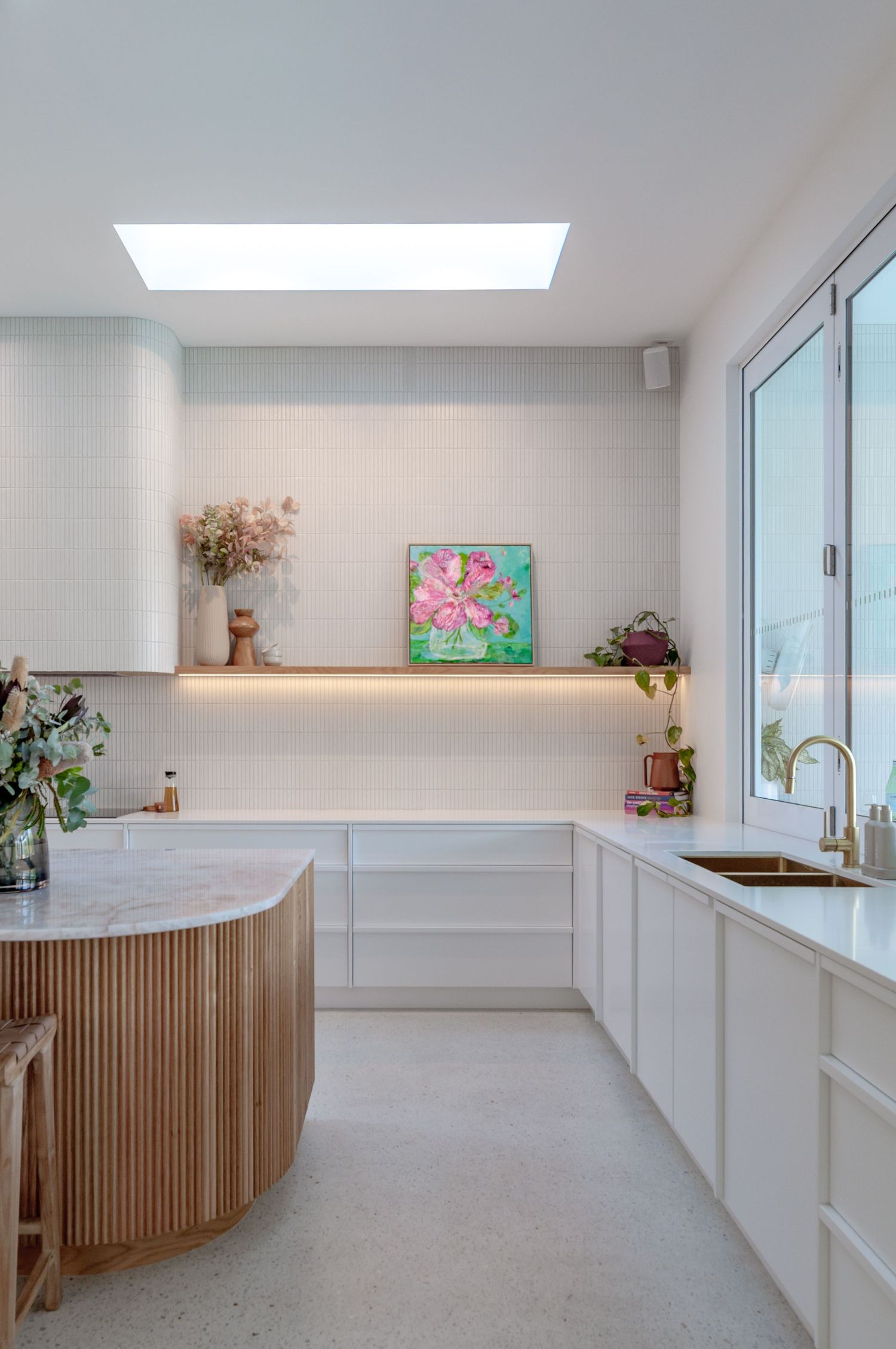 Modern white kitchen with wooden slat details, skylight, and minimalist design features floating cabinets and clean lines.