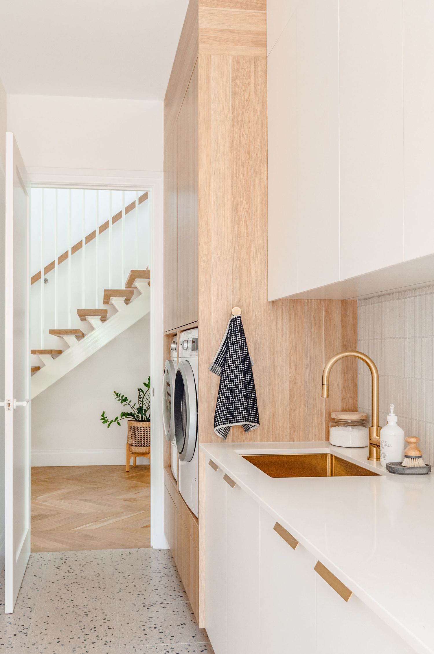 Modern minimalist kitchen with light wood accents, white cabinets, and brushed gold fixtures features terrazzo flooring.