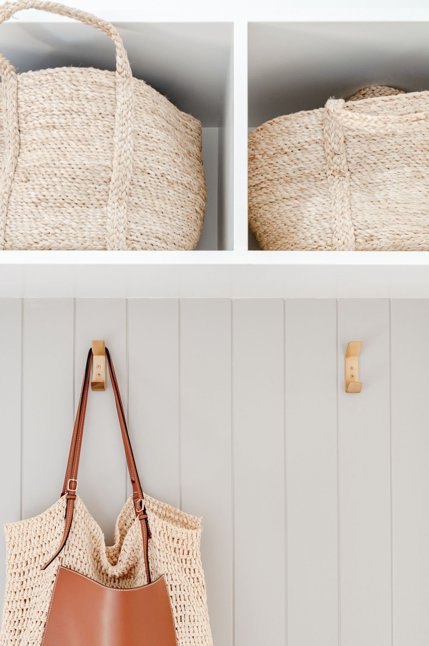 Woven storage baskets and a leather handbag hanging on white paneled wall hooks.