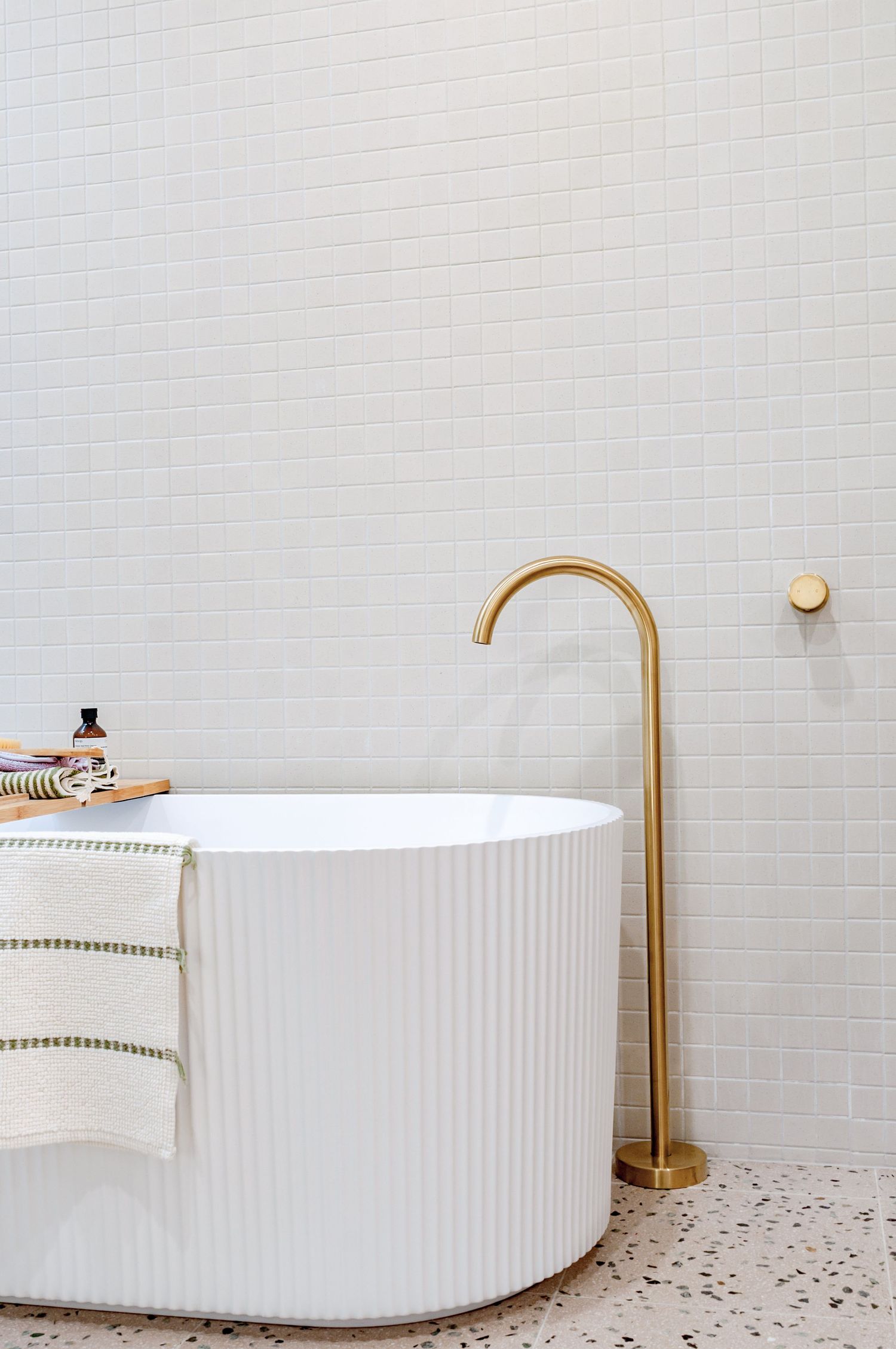 Modern white bathroom featuring a cylindrical freestanding tub with brass faucet and terrazzo flooring.