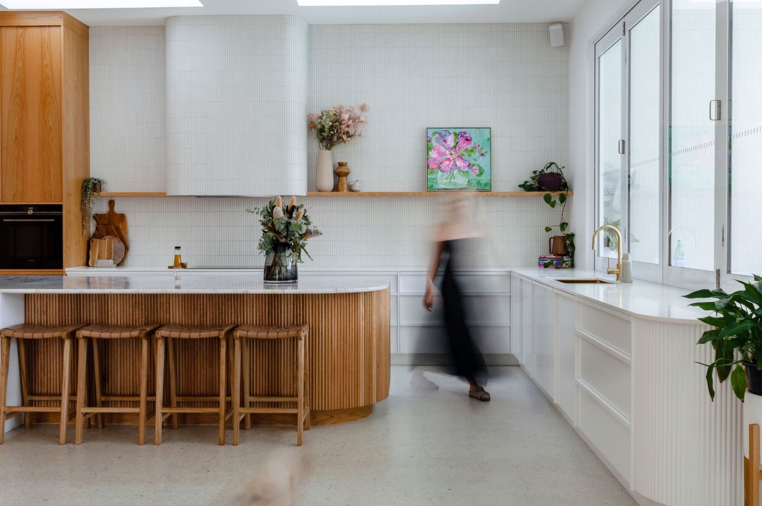 Modern bright kitchen interior with wooden cabinets, white countertops and a blurred figure walking through the space.