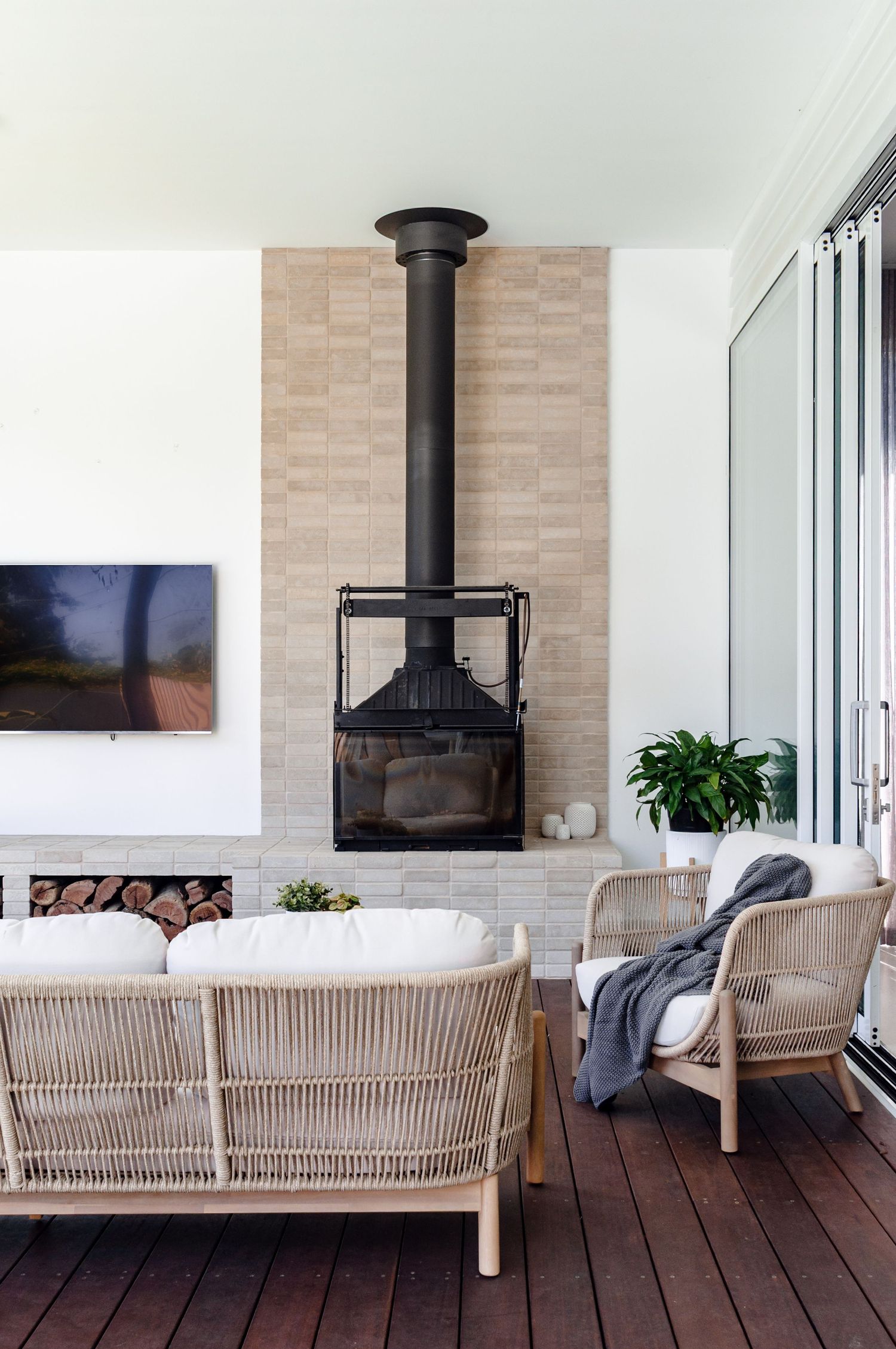 Contemporary living space with wood deck, rattan furniture, and modern black fireplace against brick wall.