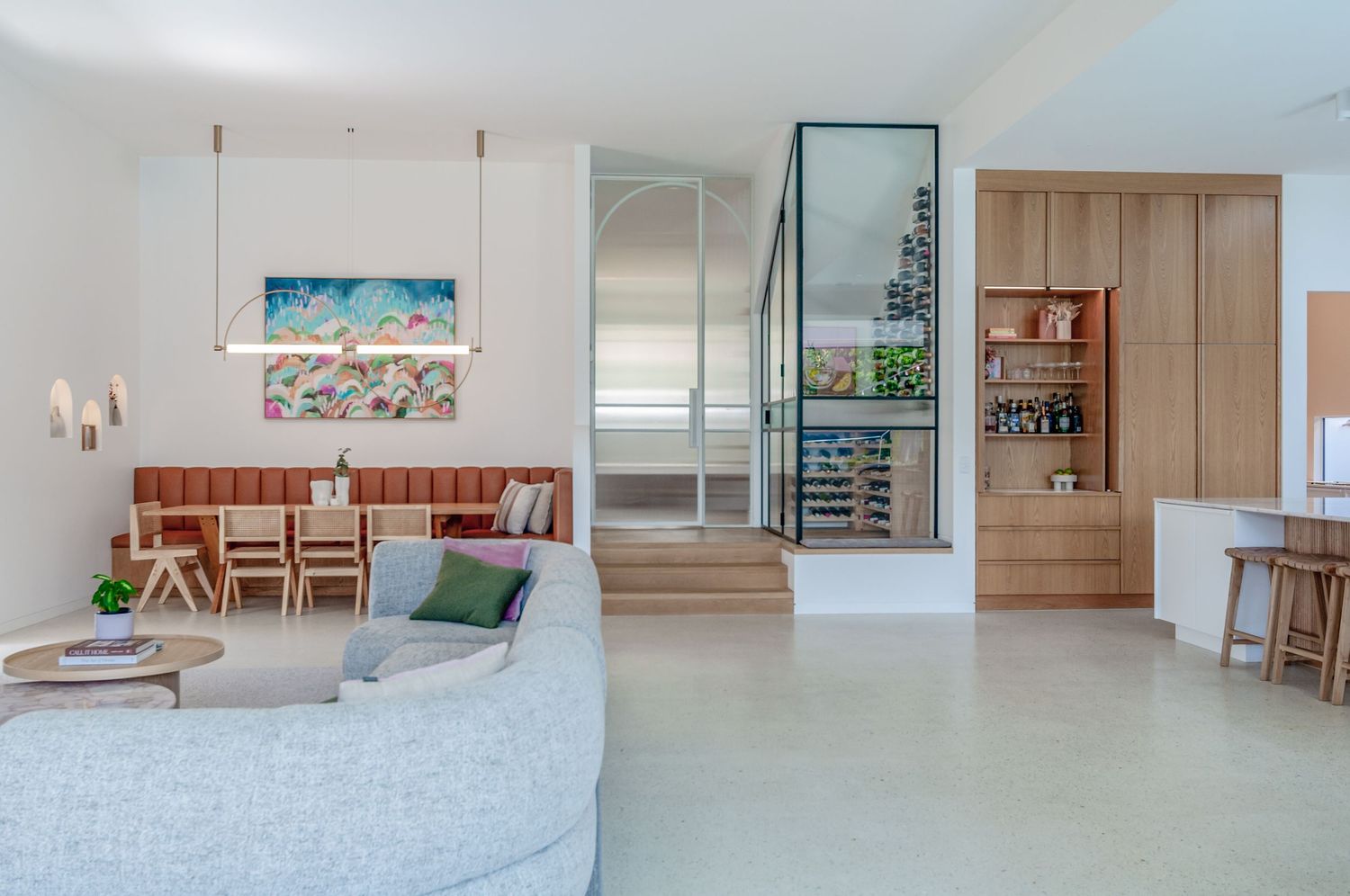 Modern coastal living room with curved sofa, wooden furniture, and vibrant beach artwork in a bright, open space.