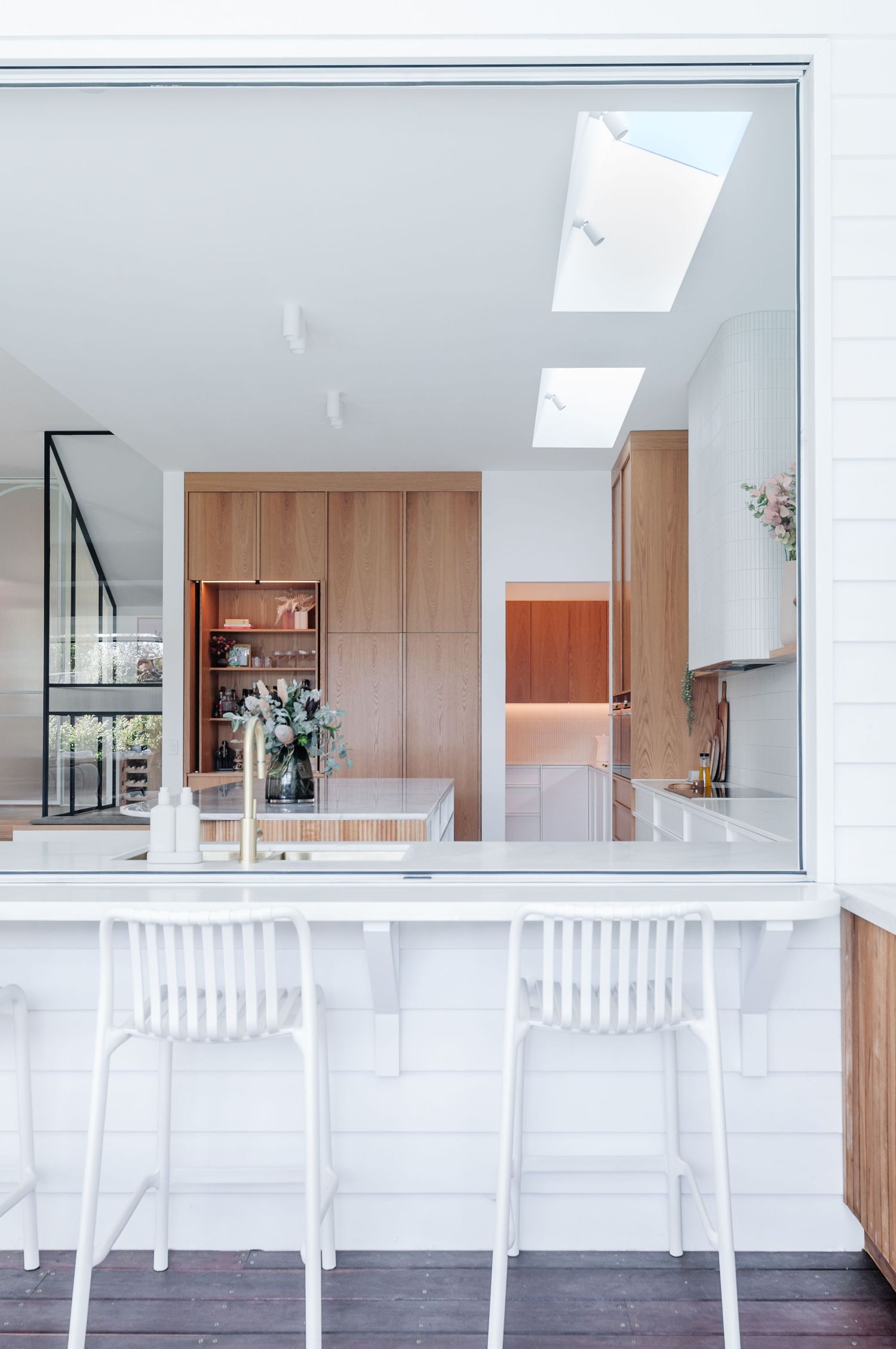 Contemporary kitchen with white bar stools, skylights, and warm wood cabinetry featuring a vase of flowers on the counter.