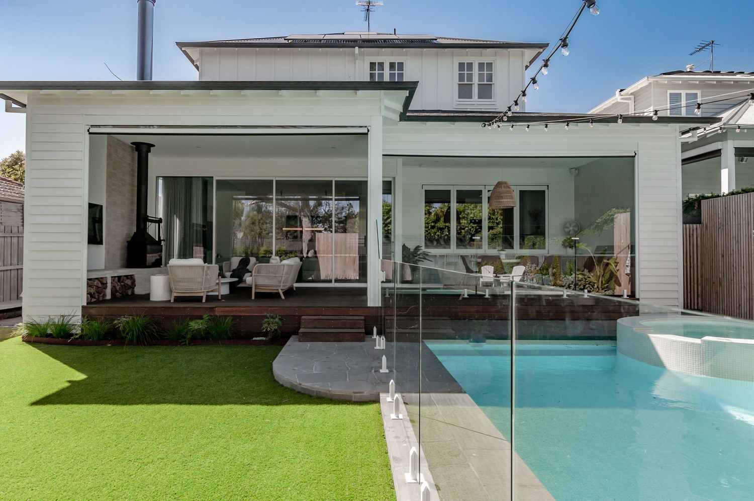 Modern white house extension with glass pool fence, artificial turf lawn and contemporary outdoor living space.