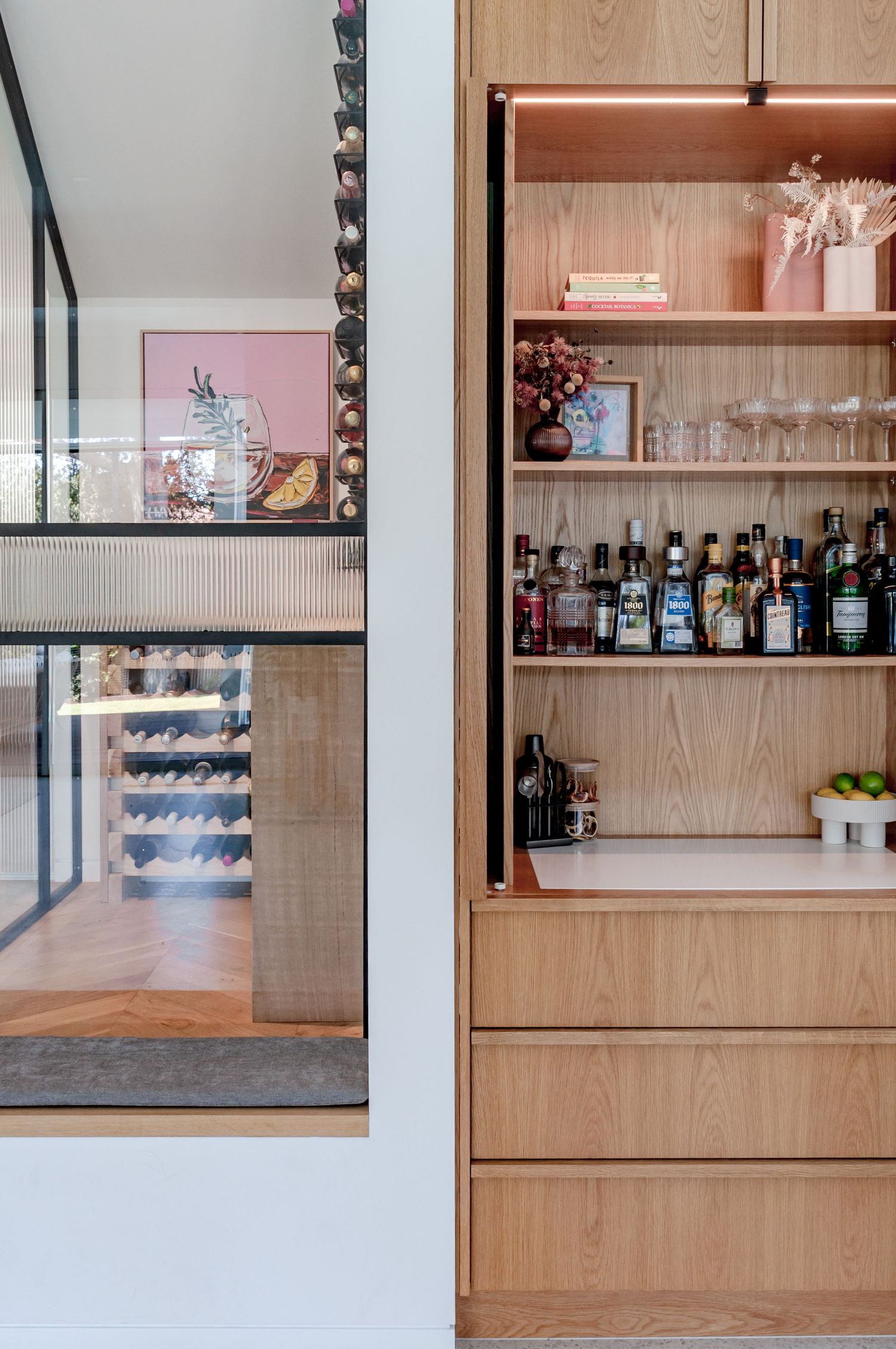 Modern wooden bar shelving displays various liquor bottles against white walls with sleek black framed accents.