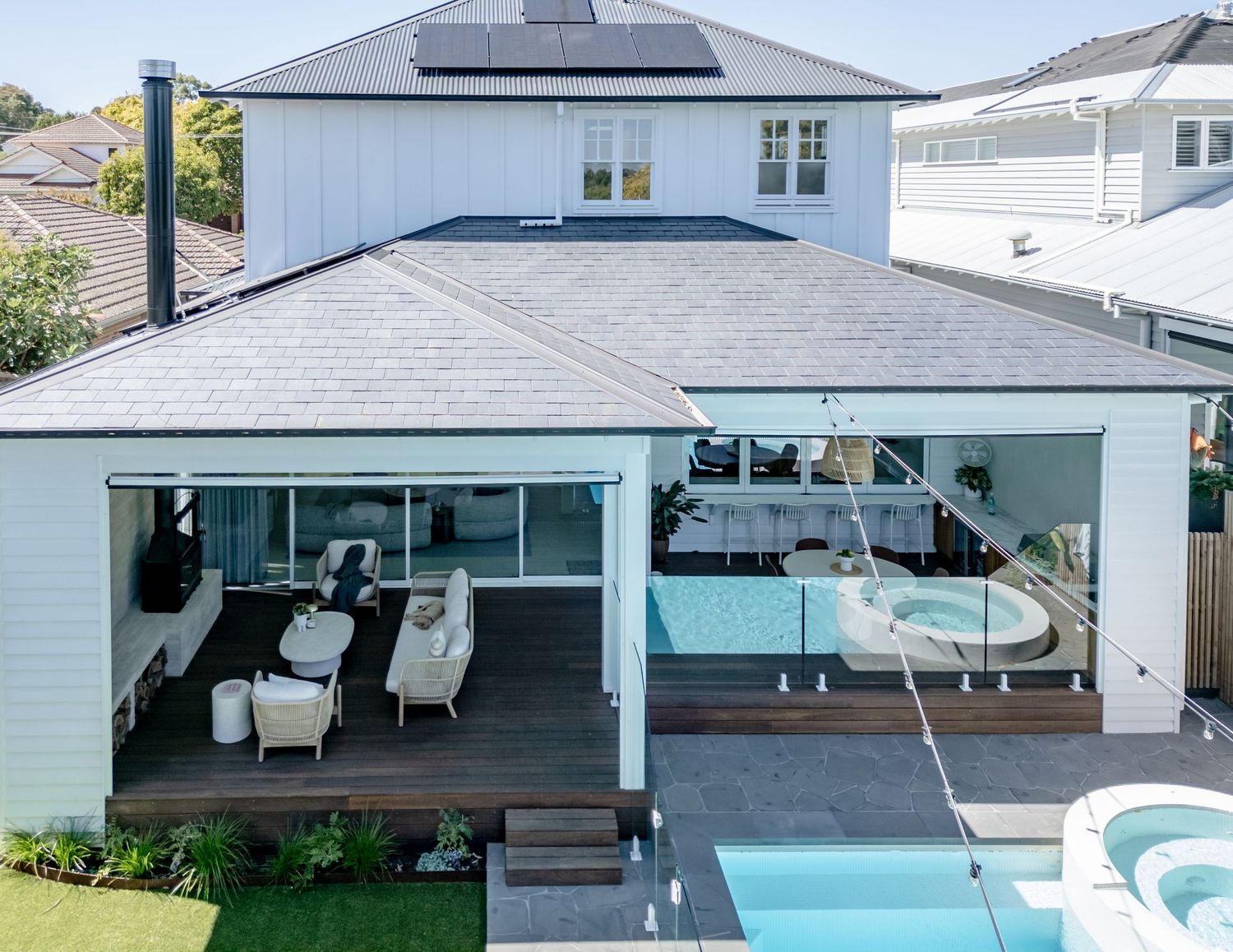 Modern coastal home with covered patio, outdoor furniture, and swimming pool featuring solar panels on the gray roof.