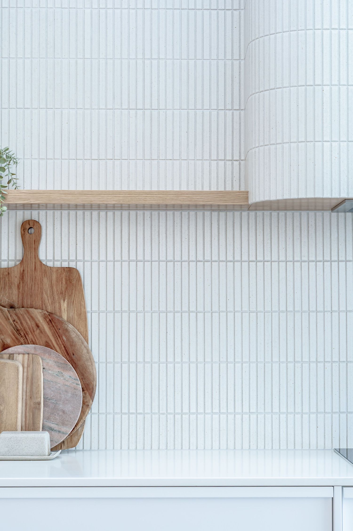 Minimalist white tile backsplash with vertical pattern complements wooden cutting boards on kitchen counter.