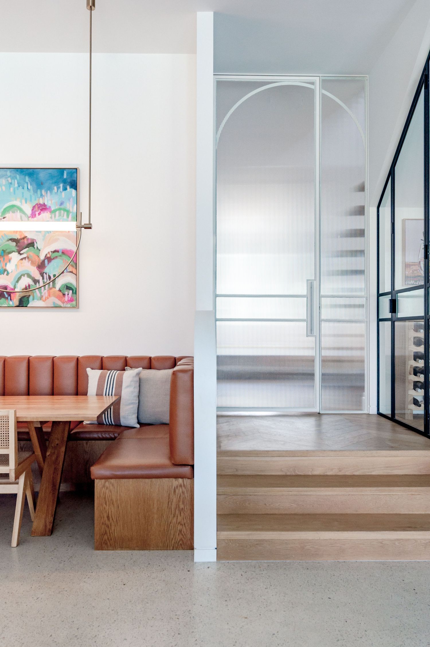 Modern interior featuring a leather banquette seating area with colorful wall art and white spiral staircase.