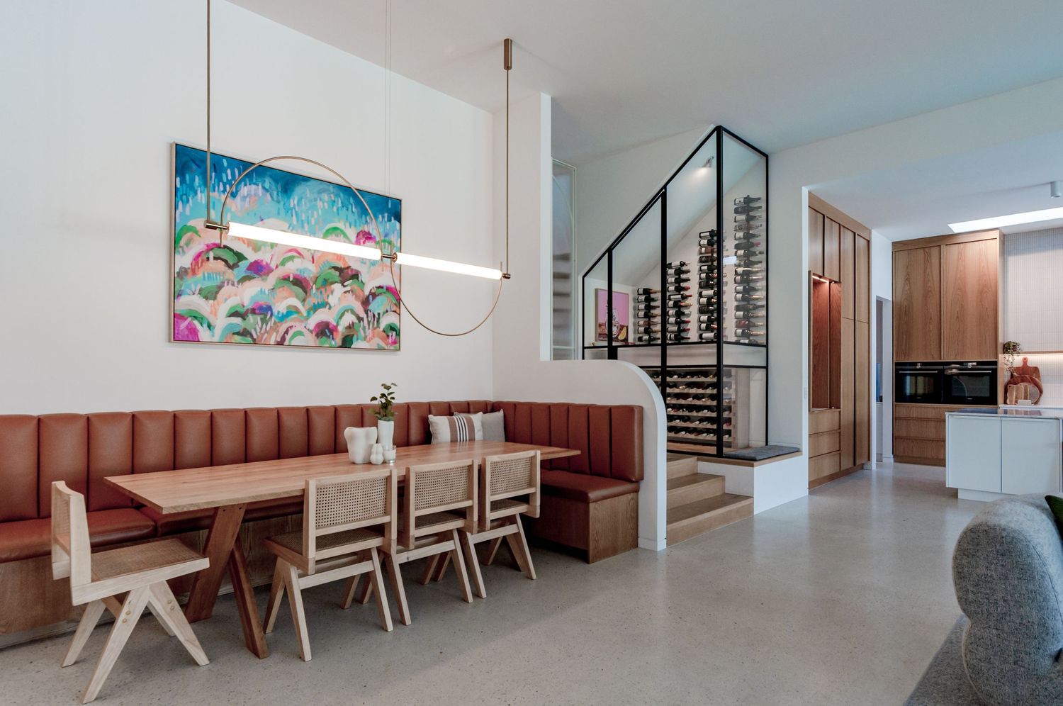 Modern dining area features plush salmon-colored banquette seating, light wood chairs, and spiral staircase in an airy space.