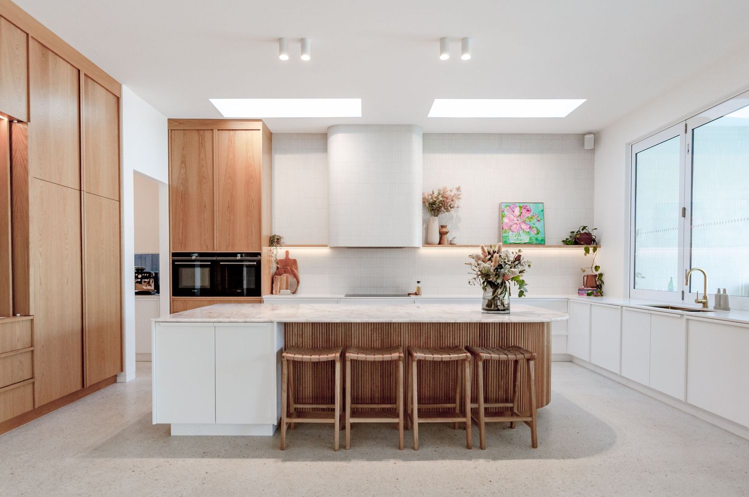 Bright modern kitchen with white cabinets, wooden bar stools, and warm wood accents throughout the space.