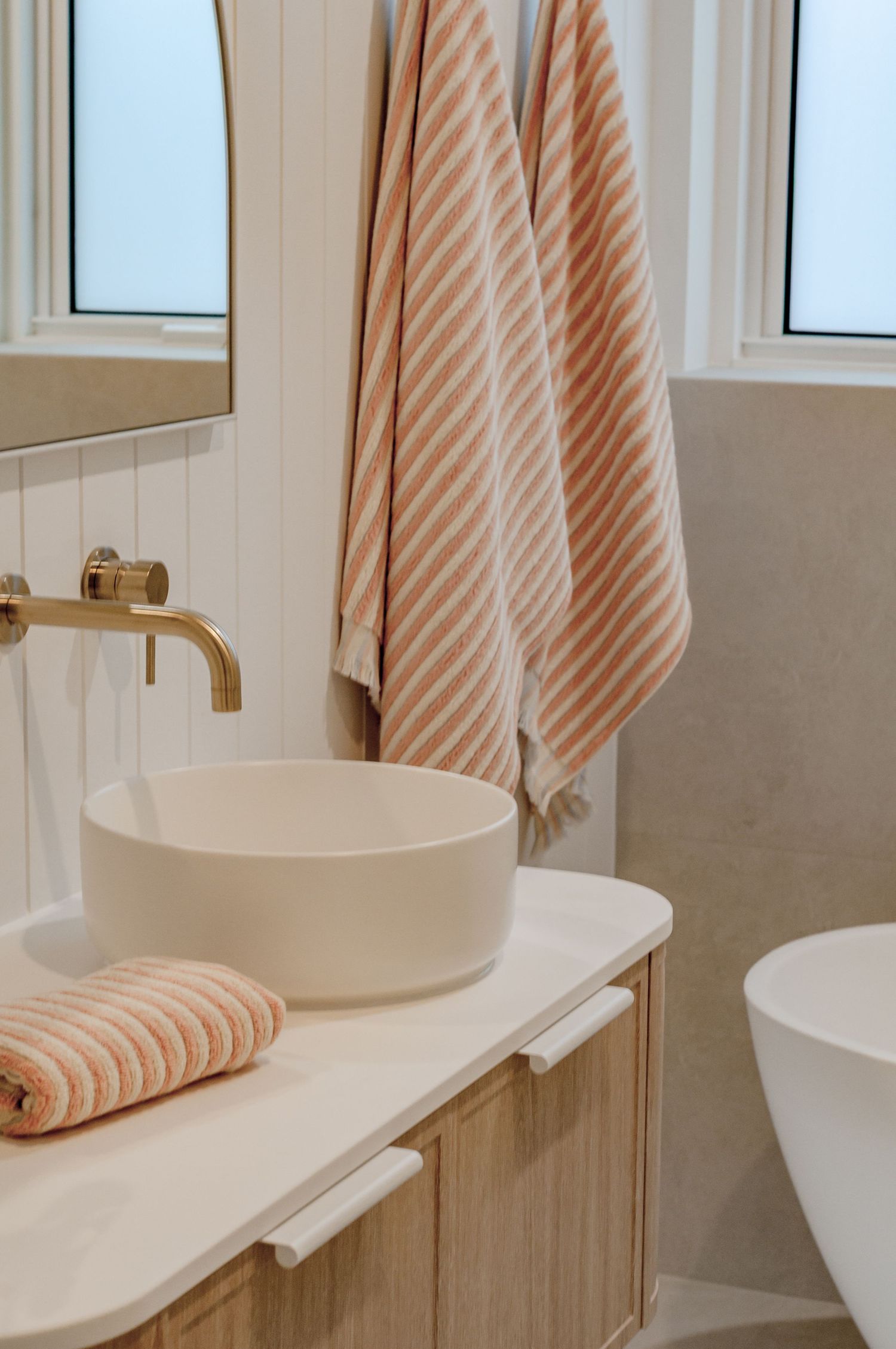 Contemporary bathroom with peach striped towels, round vessel sink, and brass wall-mounted faucet.