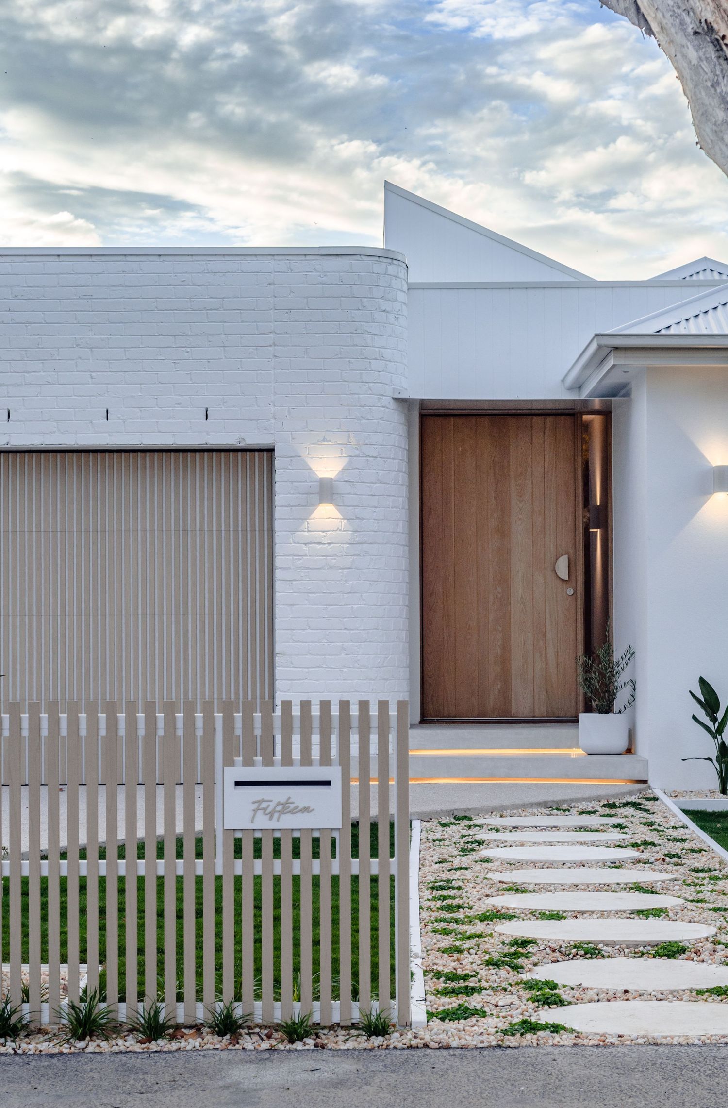 Contemporary white house exterior with wooden door, vertical slat fence, and stepping stone pathway.