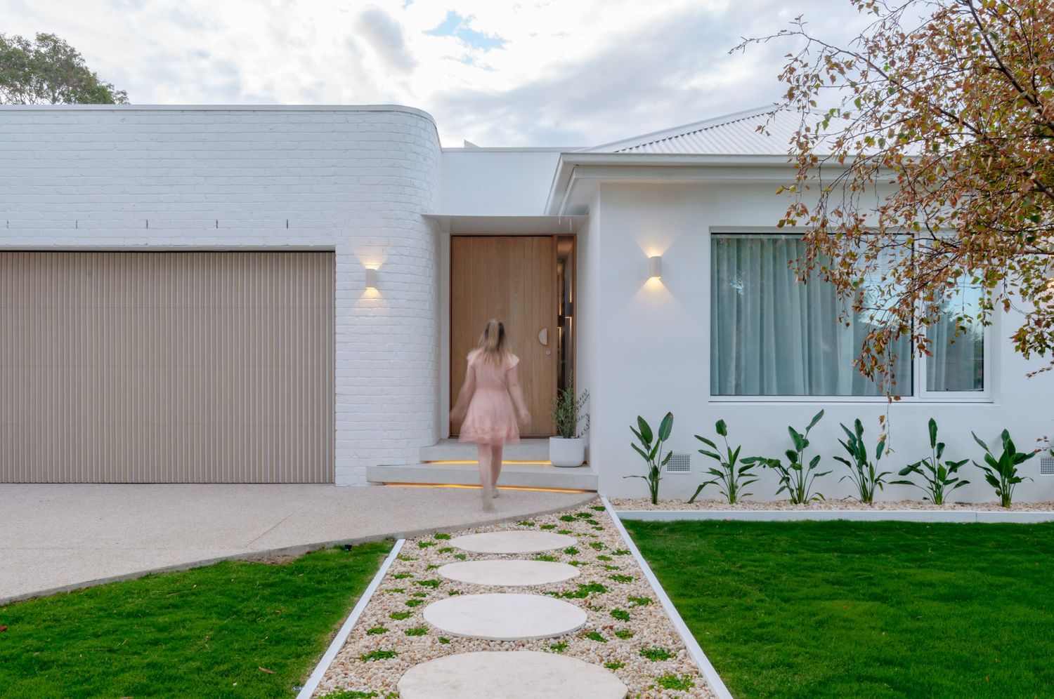Modern white house exterior with stepping stone pathway, landscaped lawn, and taupe garage door.