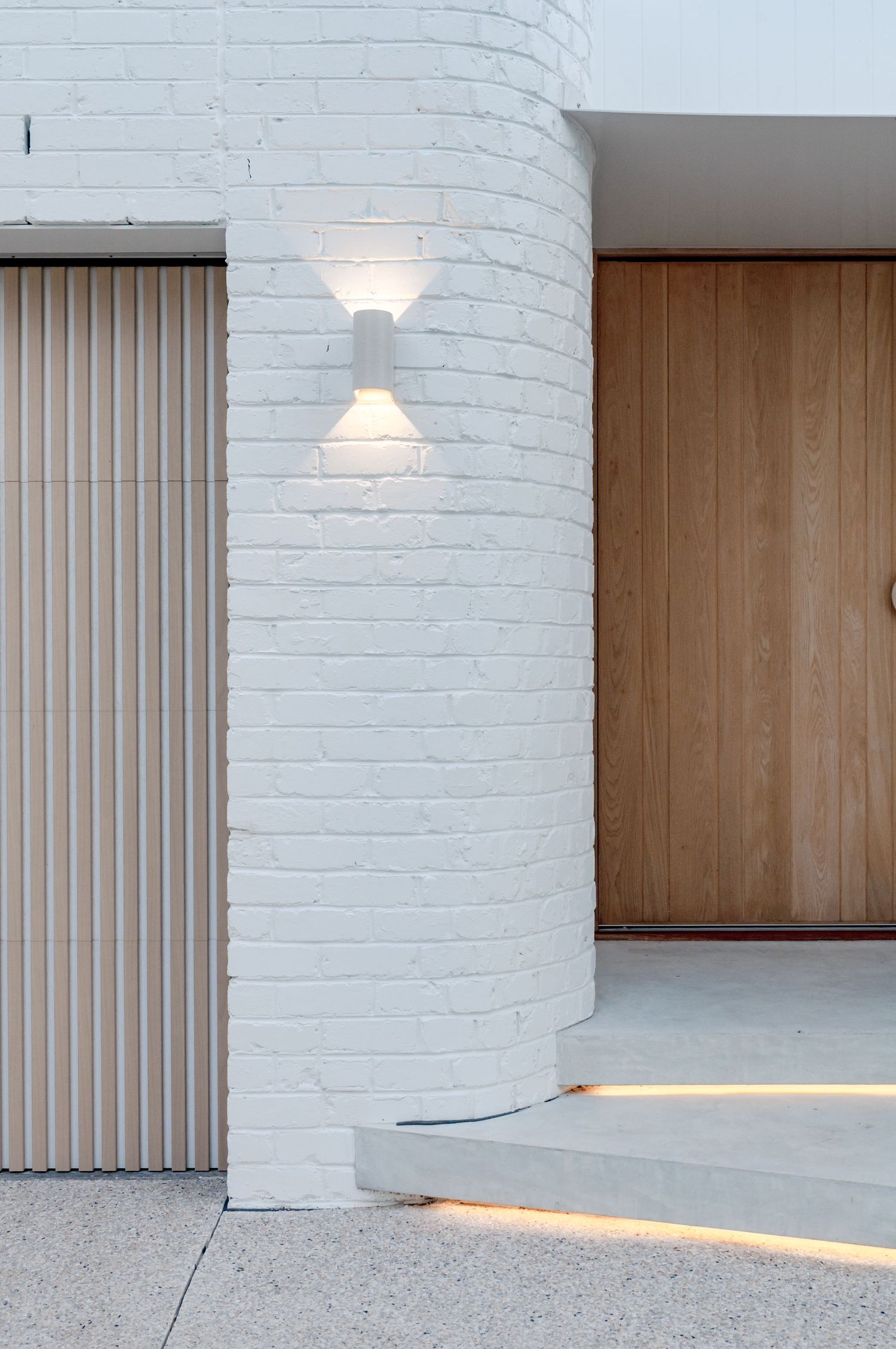 Contemporary white brick curved wall with sconce lighting and wooden slat door details.