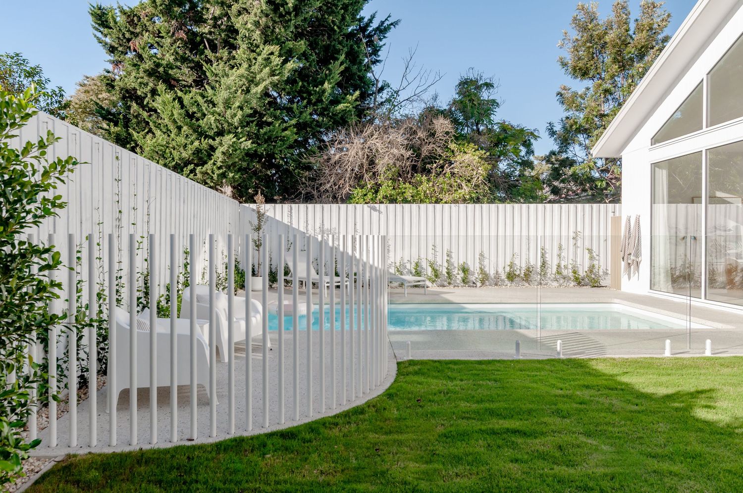 Curved white fence creating a modern boundary around a backyard pool with landscaping.