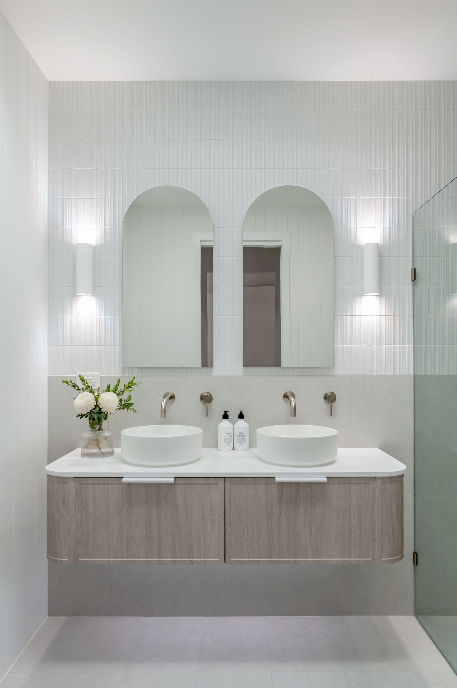 Elegant bathroom with dual arched mirrors, vessel sinks, and wood vanity against white tiled walls.