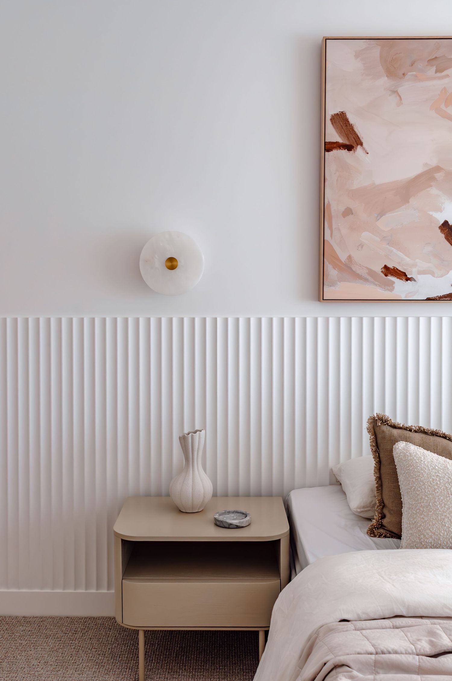 Minimalist bedroom interior with textured white wall panels, modern bedside table, and pink artwork with birds.