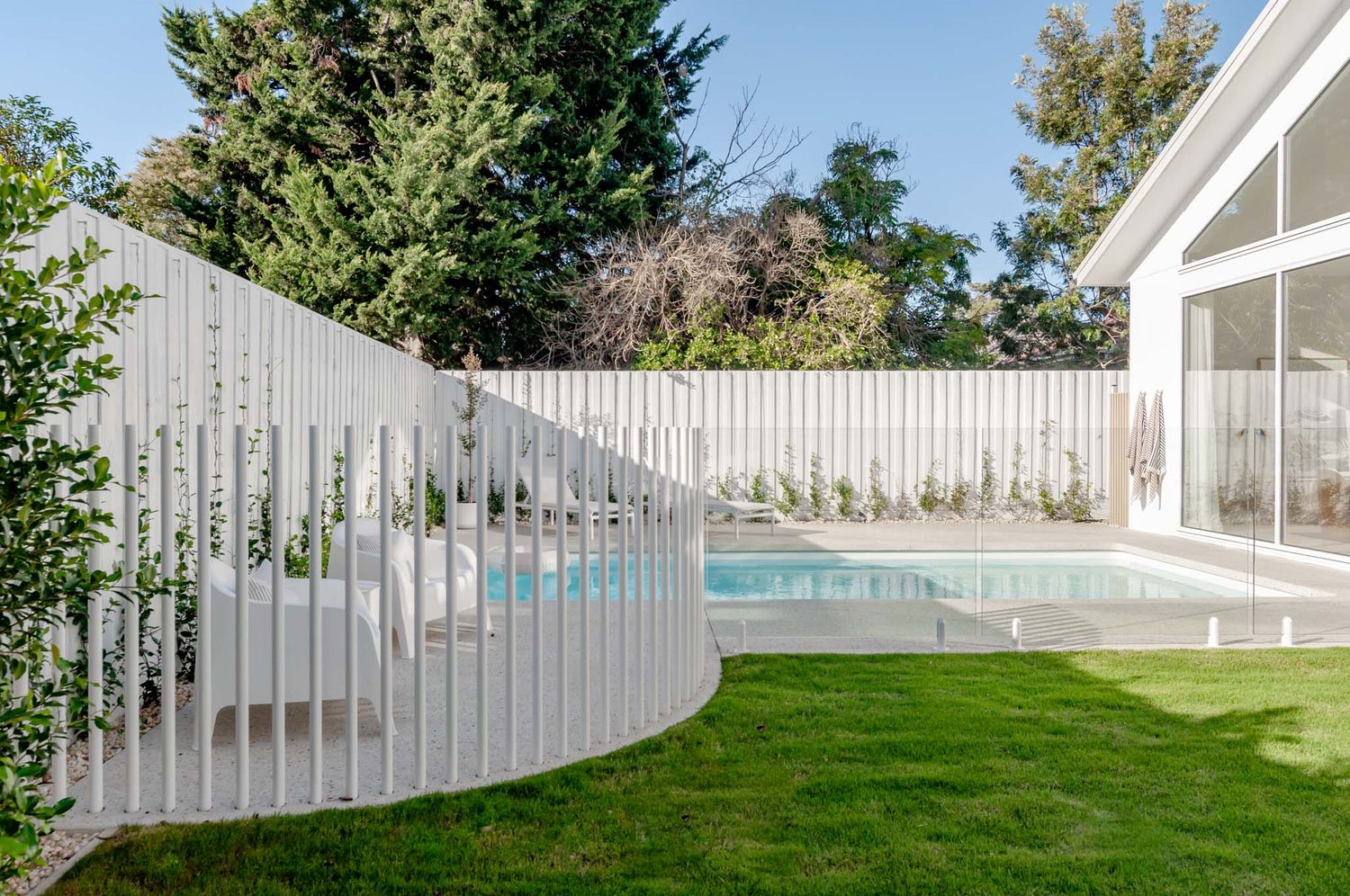 Modern curved white fence creates privacy for backyard pool area with landscaped lawn.