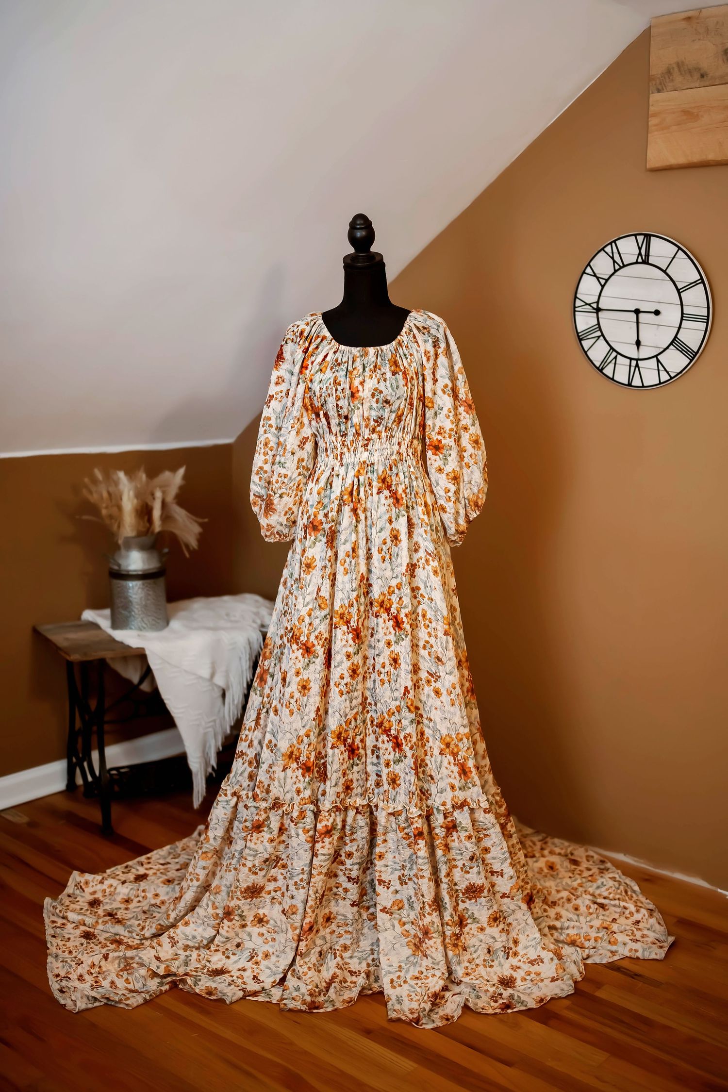 A vintage-style floral maxi dress with puff sleeves and ruffle tiers displayed on a black mannequin against a brown wall.