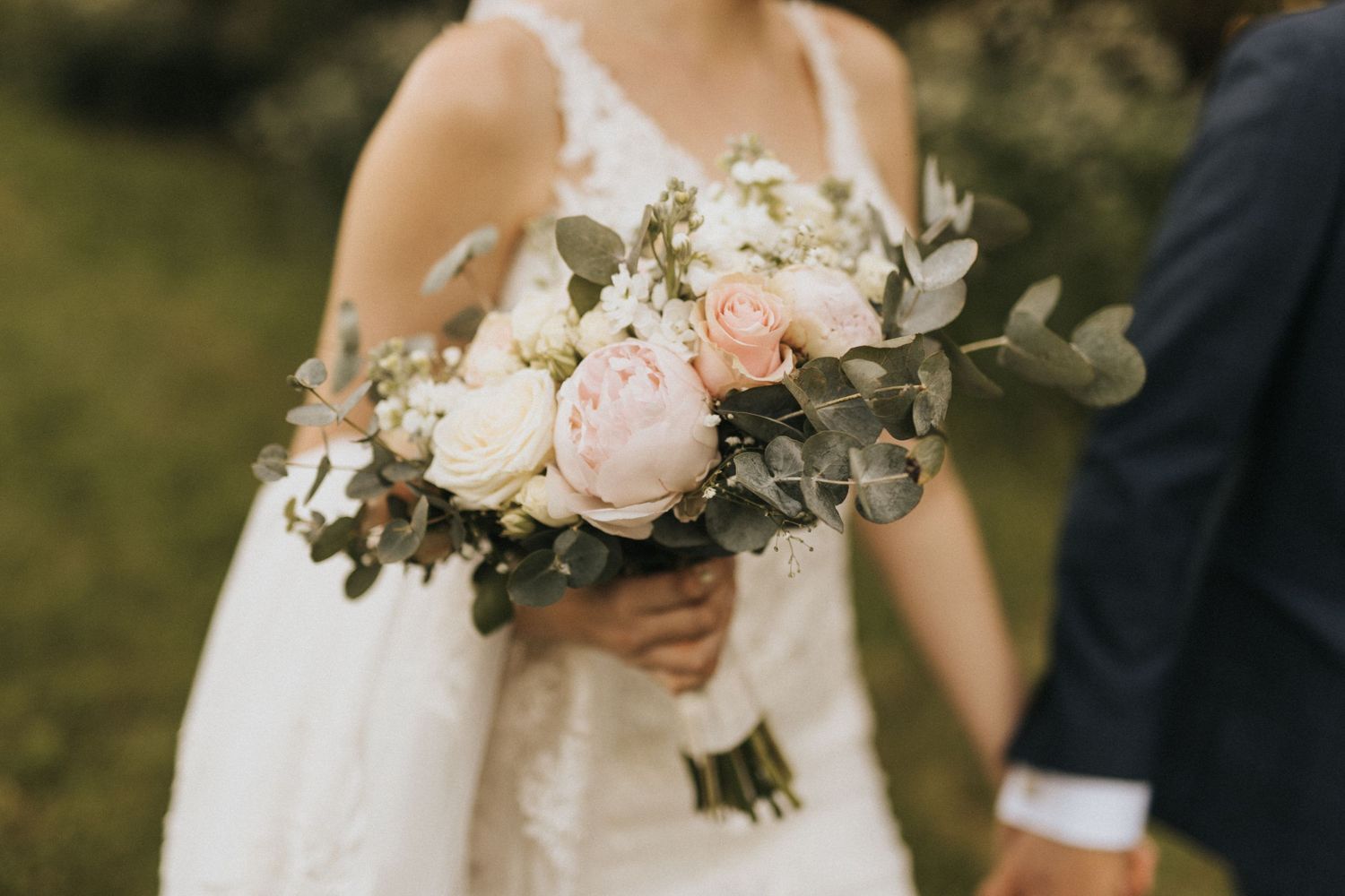 A romantic wedding bouquet featuring blush pink and white roses with silvery eucalyptus leaves against a white dress.