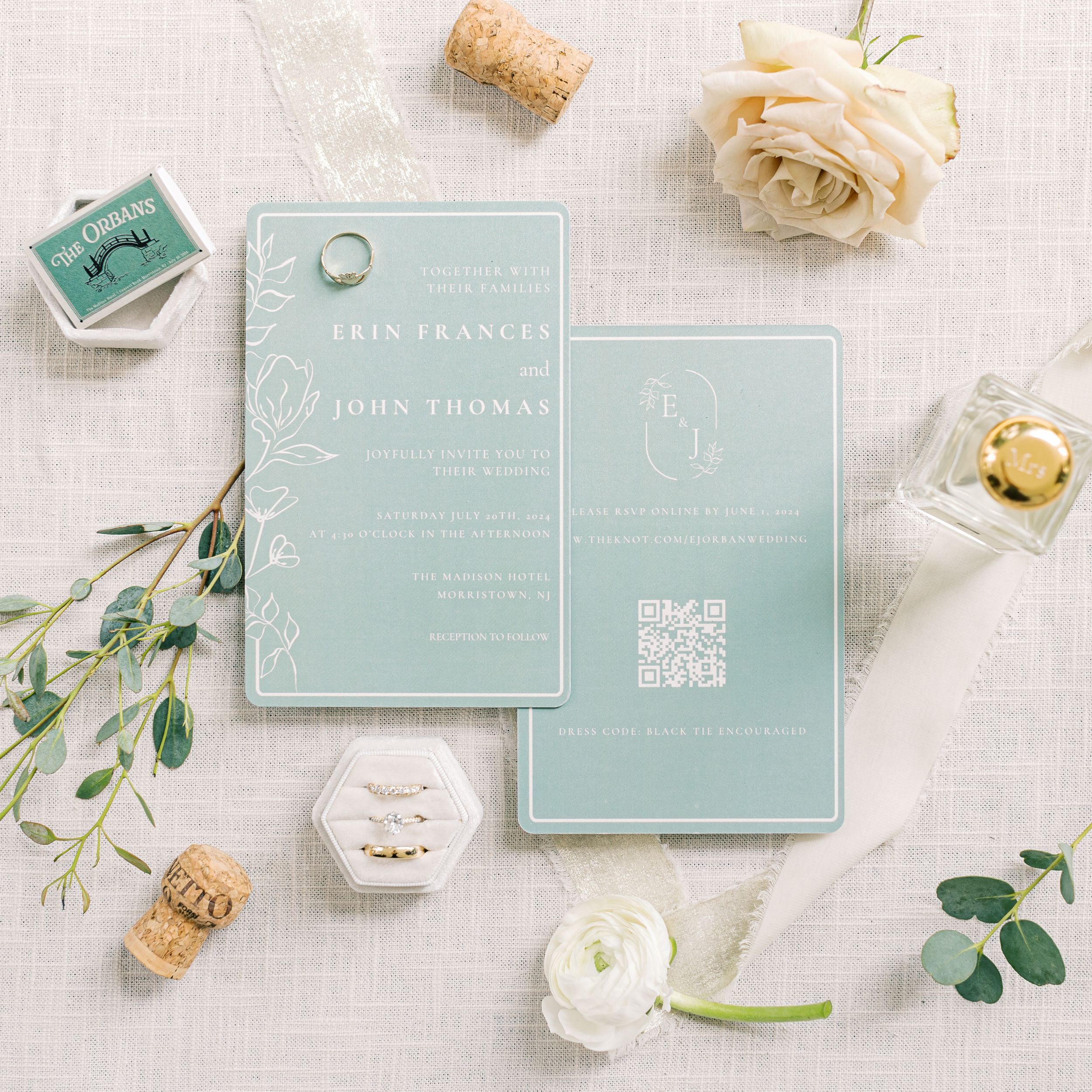 Elegant mint green wedding invitations with QR code displayed with white roses, champagne corks and eucalyptus leaves.