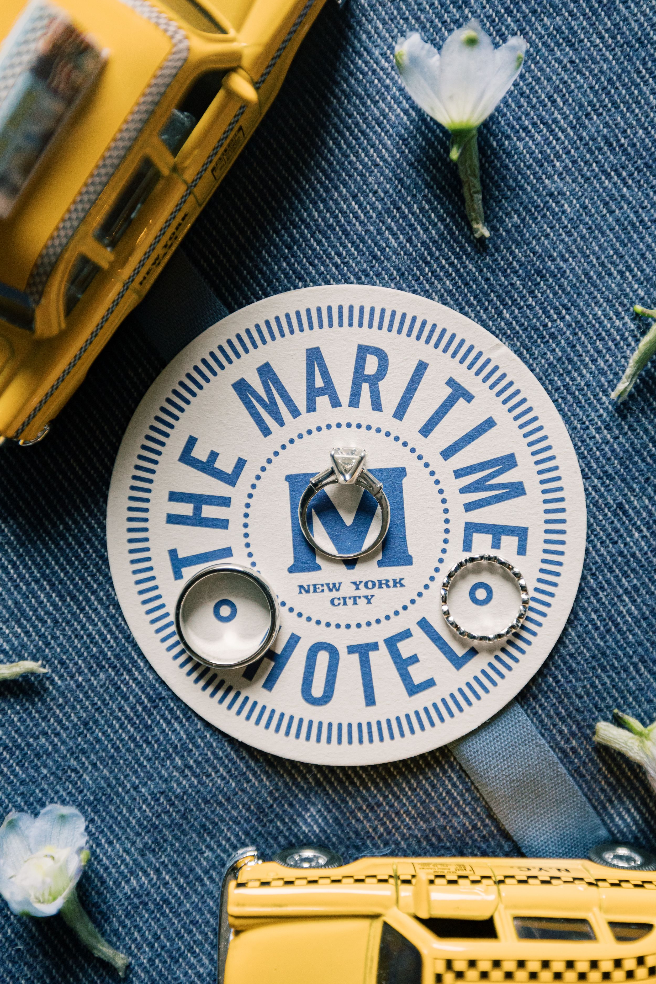 White and blue vintage Maritime Hotel pins scattered on denim fabric with yellow toy buses and crystal accents.