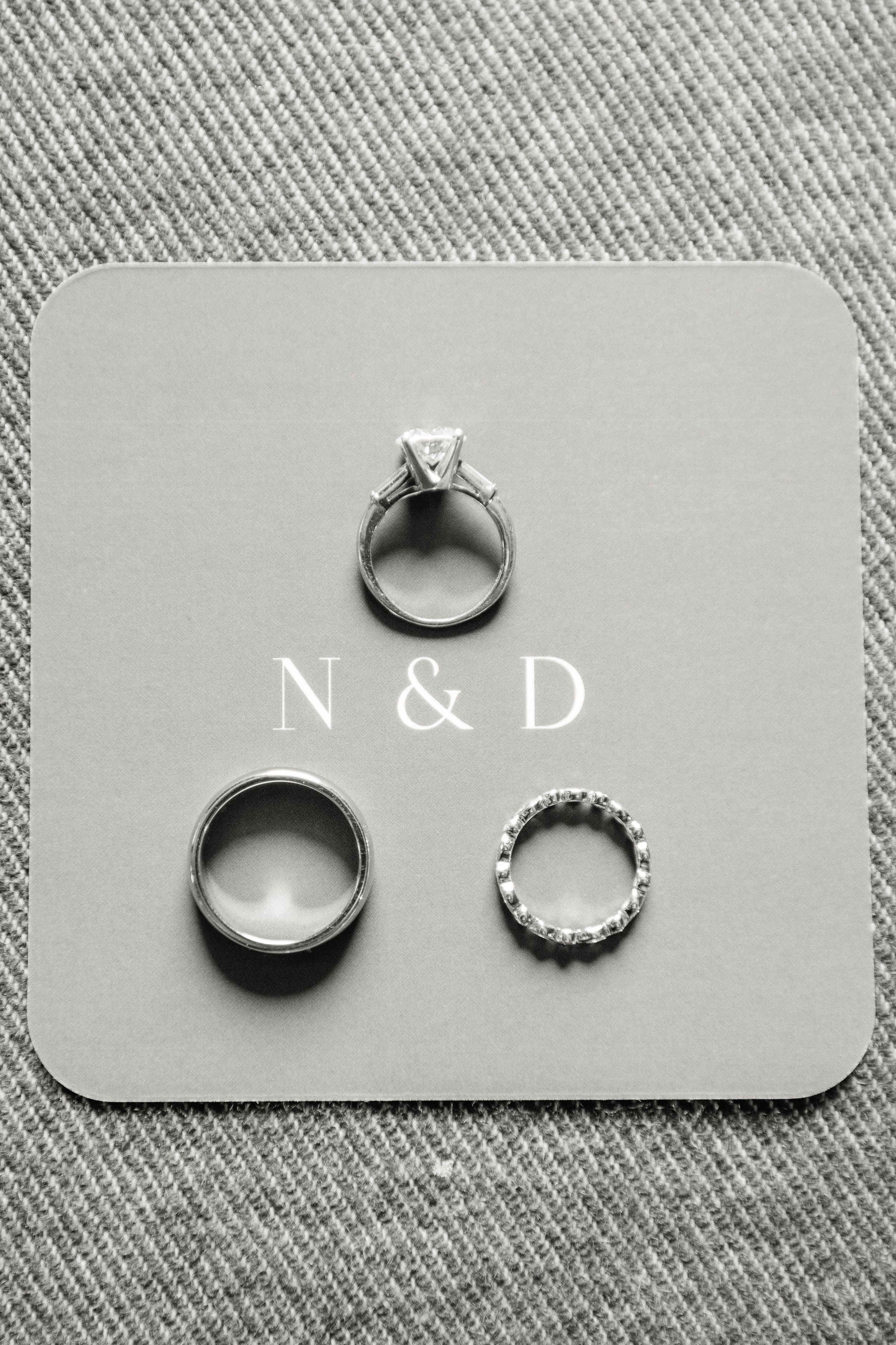 Wedding rings displayed on gray card with initials N & D, featuring an engagement ring with diamond and two bands.