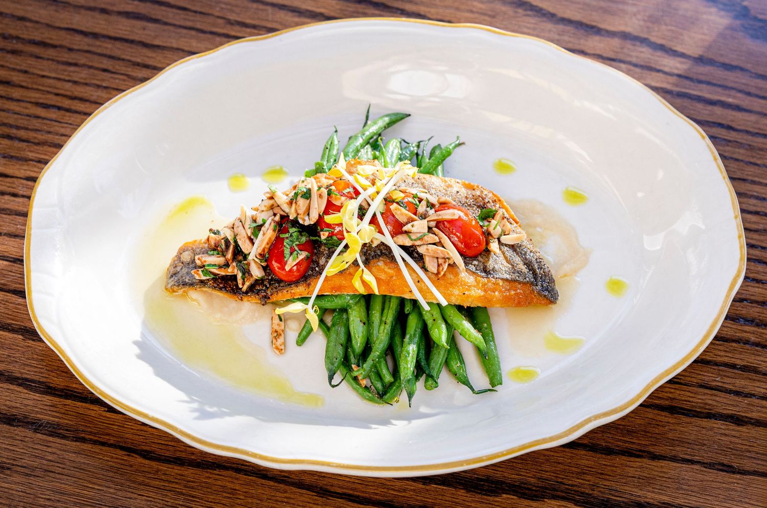 Elegantly plated dishes arranged in a row on white plates showcase various gourmet preparations on a wooden table.