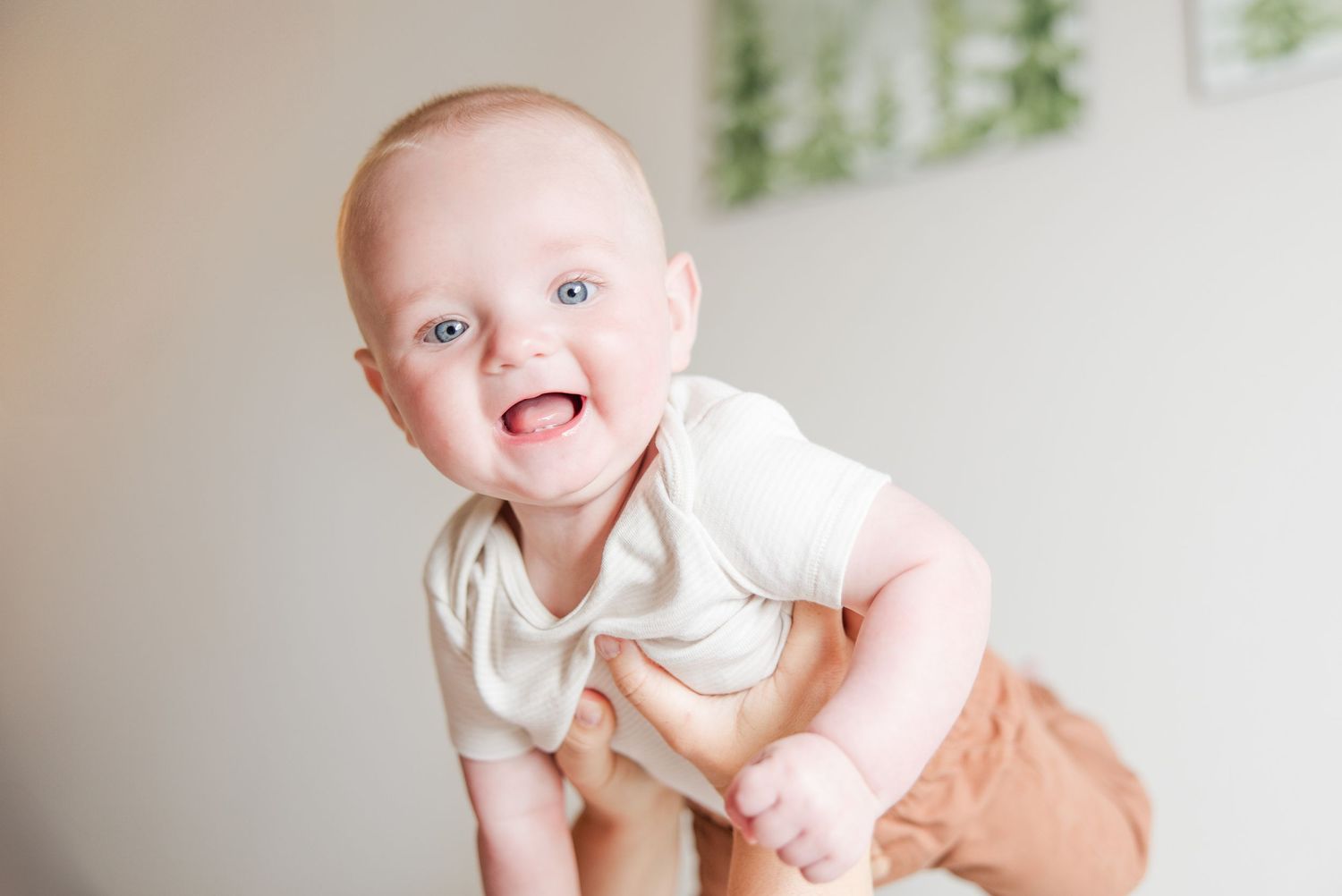 Happy baby in a white onesie laughing and playing during an indoor photo session.