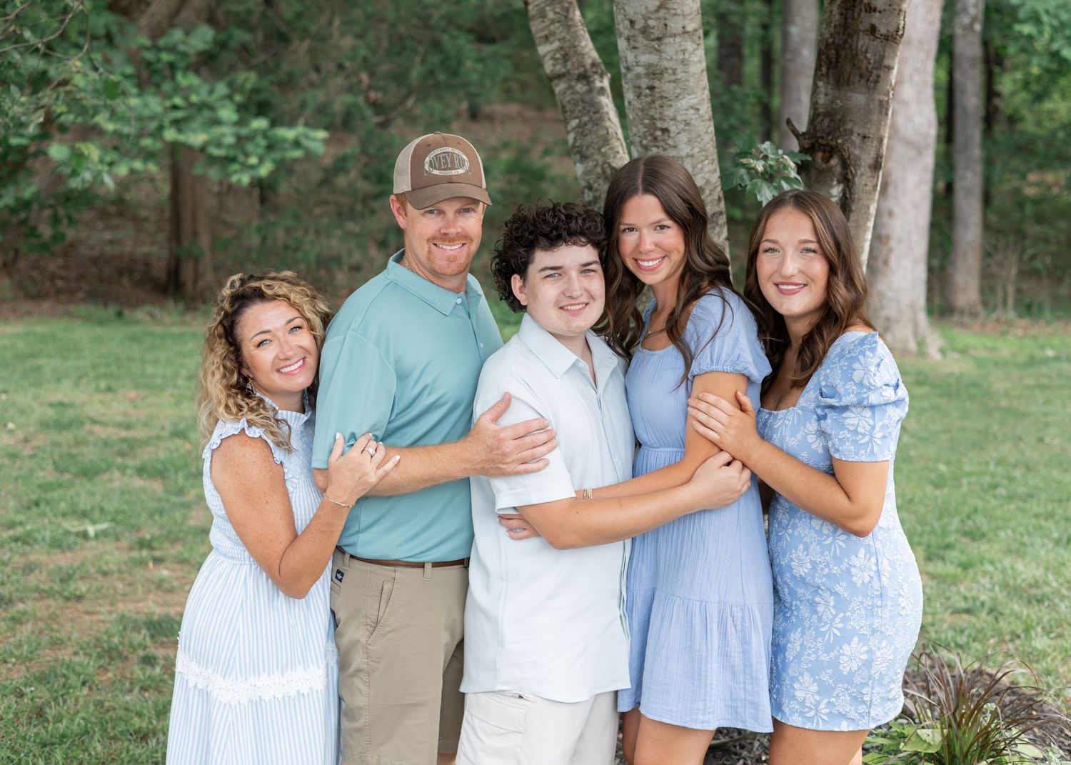 Family portrait session in a park setting with coordinated casual outfits in blue tones.