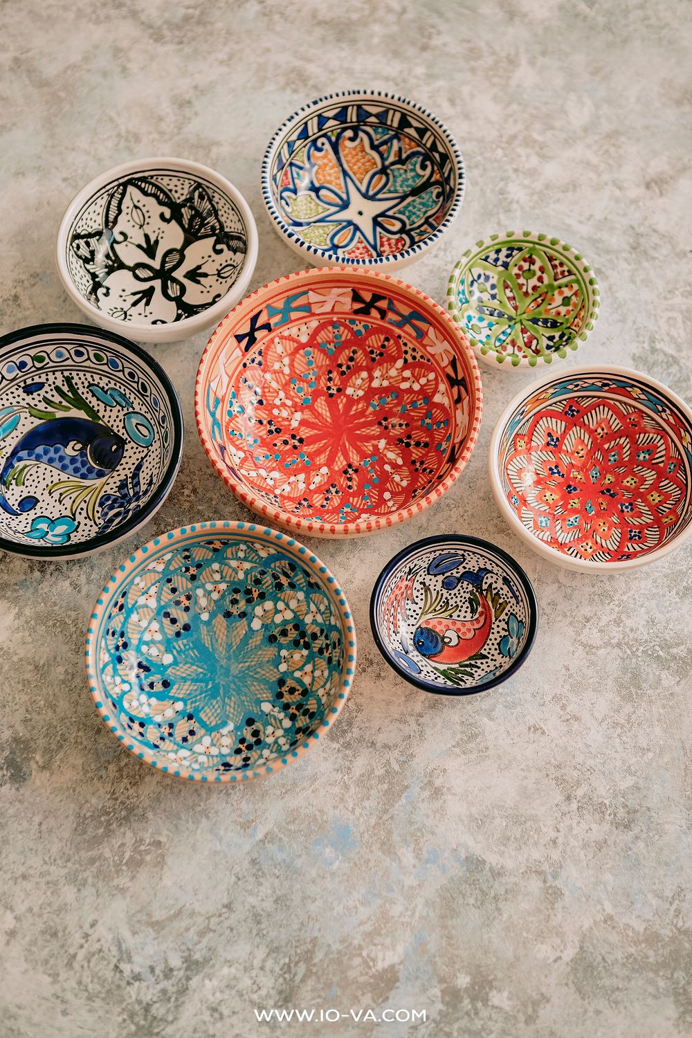 Collection of colorful hand-painted Turkish ceramic bowls with traditional floral patterns on stone surface.
