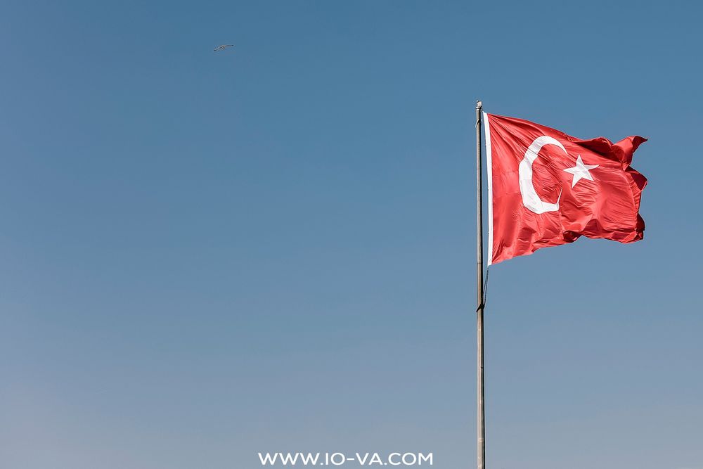 Turkish national flag with white crescent and star waving against a clear blue sky on a flagpole.