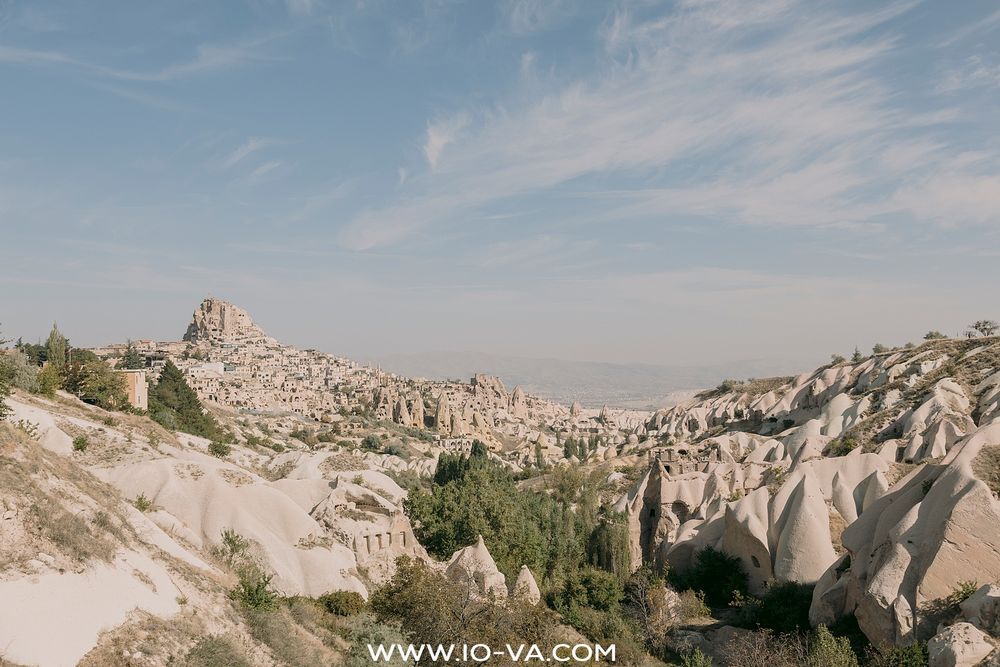 Sweeping landscape of Cappadocia's volcanic rock formations and Uchisar Castle under a blue sky in Turkey.