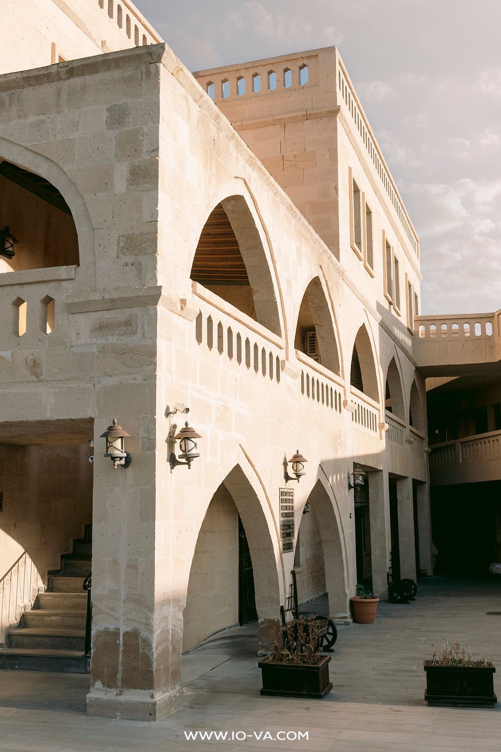 Historic stone building with arched colonnades and balconies in warm sunlight, featuring ornate lanterns.