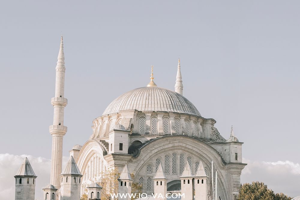 The white marble Nuruosmaniye Mosque with its dome and minarets glows under a pale blue sky.