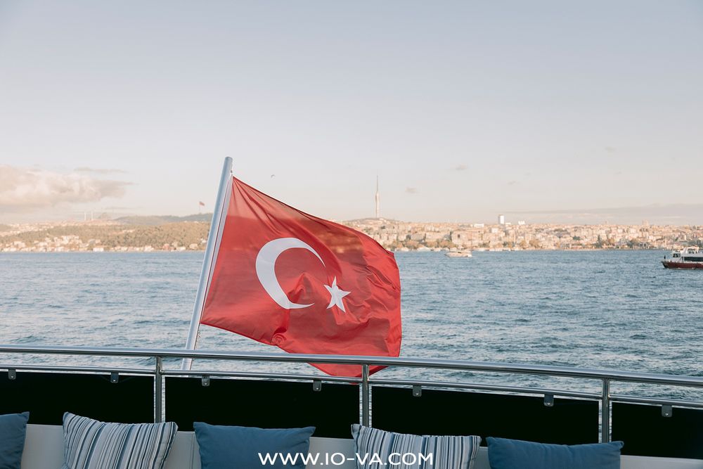 A Turkish flag waves proudly on a boat deck with the Istanbul Bosphorus skyline in the background.
