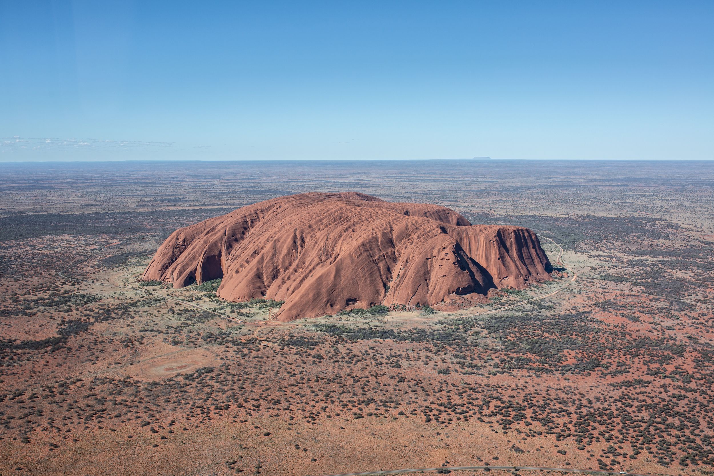 Aerial view of Uluru, a massive red sandstone rock formation rising from the Australian Outback landscape.