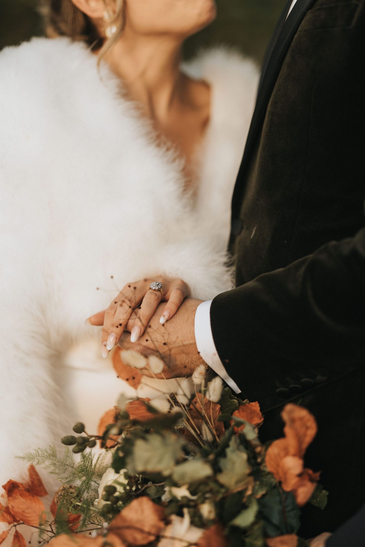 Wedding couple's footwear with brown leather dress shoes and white sandals next to a peach floral bouquet on stone ground.